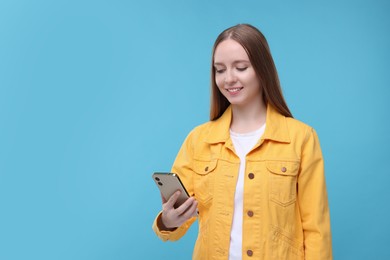 Happy woman sending message via smartphone on light blue background, space for text