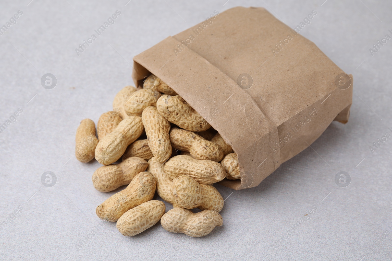 Photo of Paper bag with fresh unpeeled peanuts on grey table, closeup