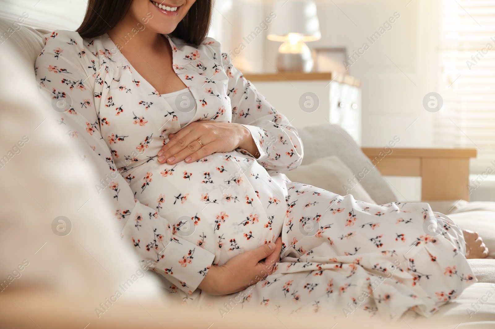 Photo of Young pregnant woman sitting on sofa at home, closeup