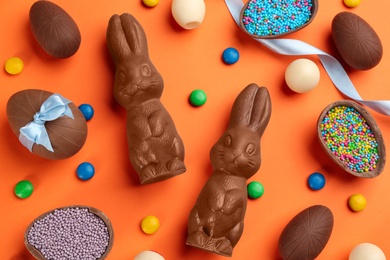 Photo of Flat lay composition with chocolate Easter bunnies, eggs and candies on orange background