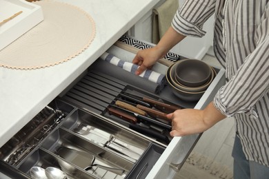 Photo of Woman taking towel from open drawer of kitchen cabinet, closeup