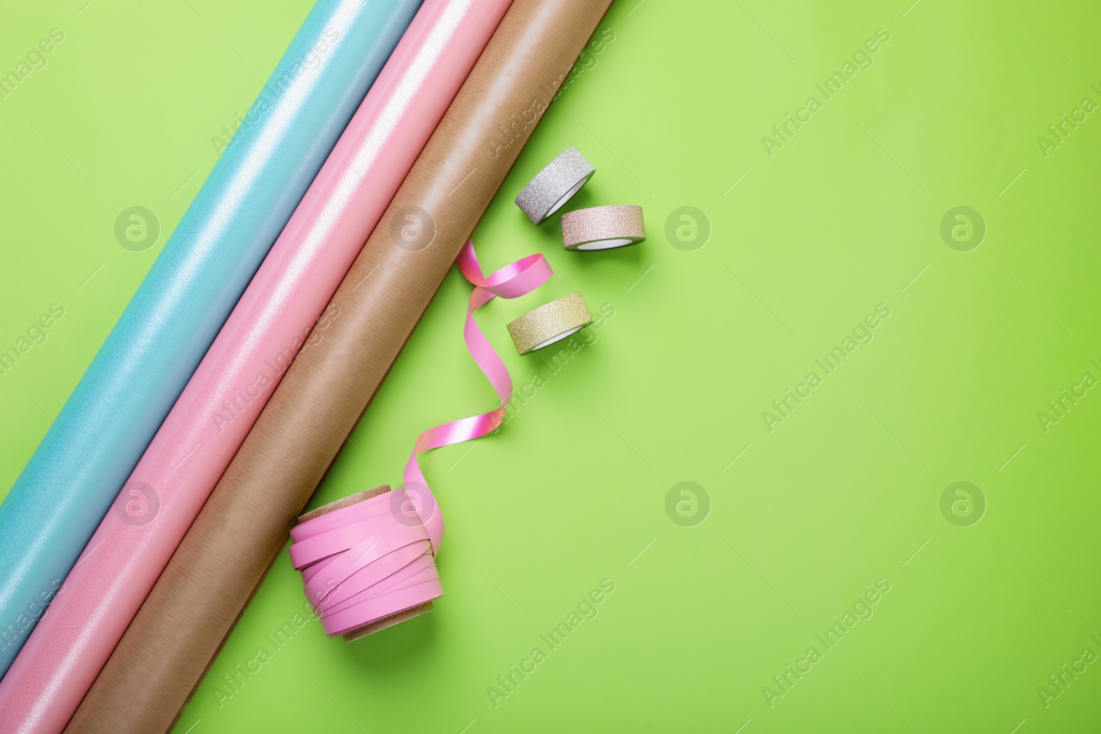 Photo of Rolls of wrapping papers and ribbons on green background, flat lay. Space for text