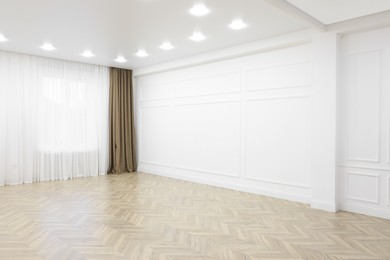 Photo of Empty room with white wall, wooden floor and spot lamps on ceiling