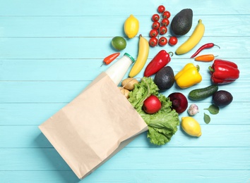 Shopping paper bag with different groceries on light blue wooden background, flat lay