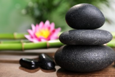 Photo of Stacked spa stones, bamboo stems and flower on wooden table against blurred background, closeup. Space for text