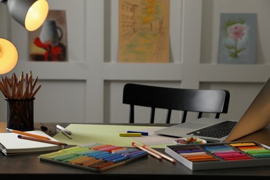 Photo of Artist's workplace with soft pastels, laptop and drawing pencils on table indoors