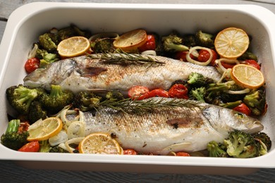 Photo of Delicious fish with vegetables and lemon in baking dish on table