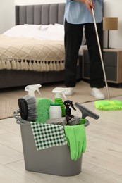 Photo of Woman cleaning floor, focus on different supplies in bucket at home