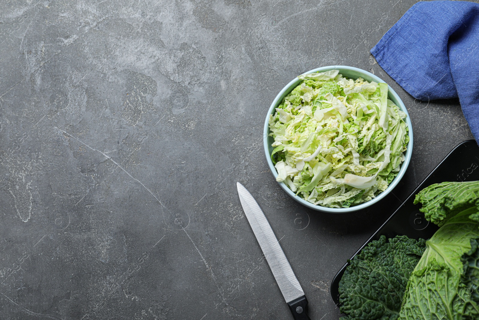 Photo of Cut fresh savoy cabbage in bowl on grey table, flat lay. Space for text