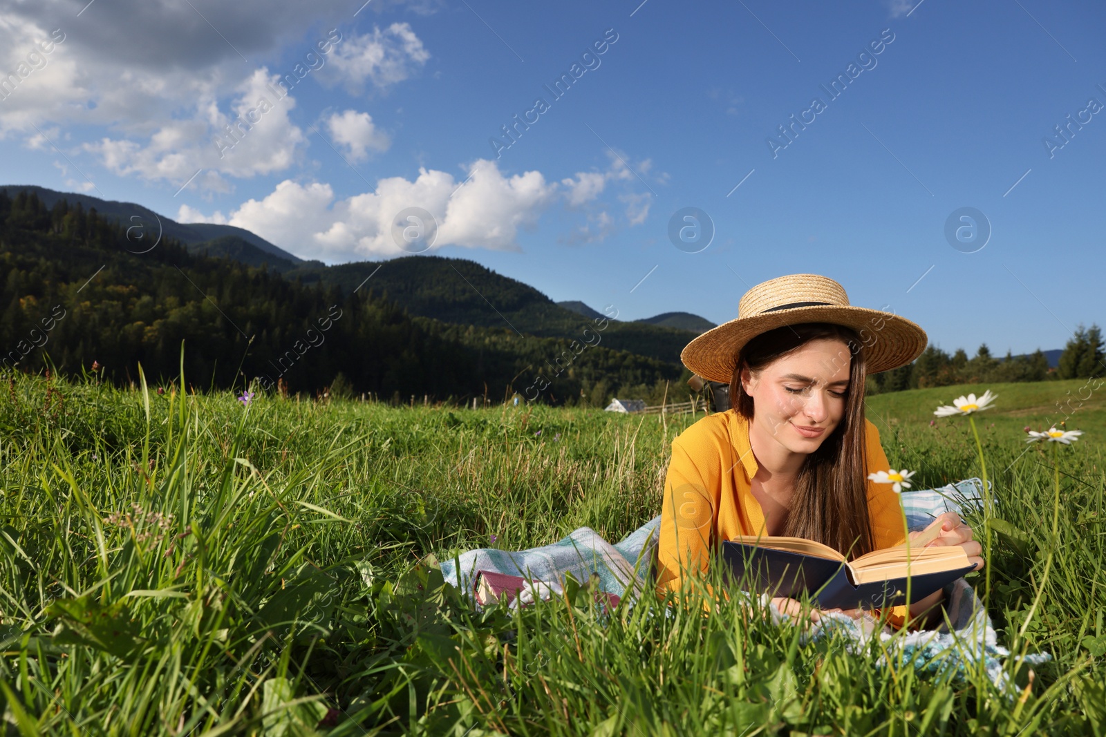 Photo of Beautiful young woman reading book on green meadow in mountains