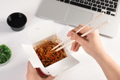 Woman eating tasty Chinese noodles at workplace, closeup. Food delivery