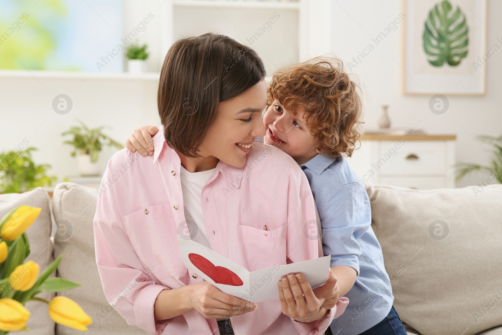 Photo of Little son congratulating his mom with Mother`s day at home. Woman holding handmade greeting card