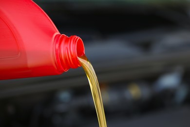 Pouring motor oil from red container against blurred background, closeup. Space for text