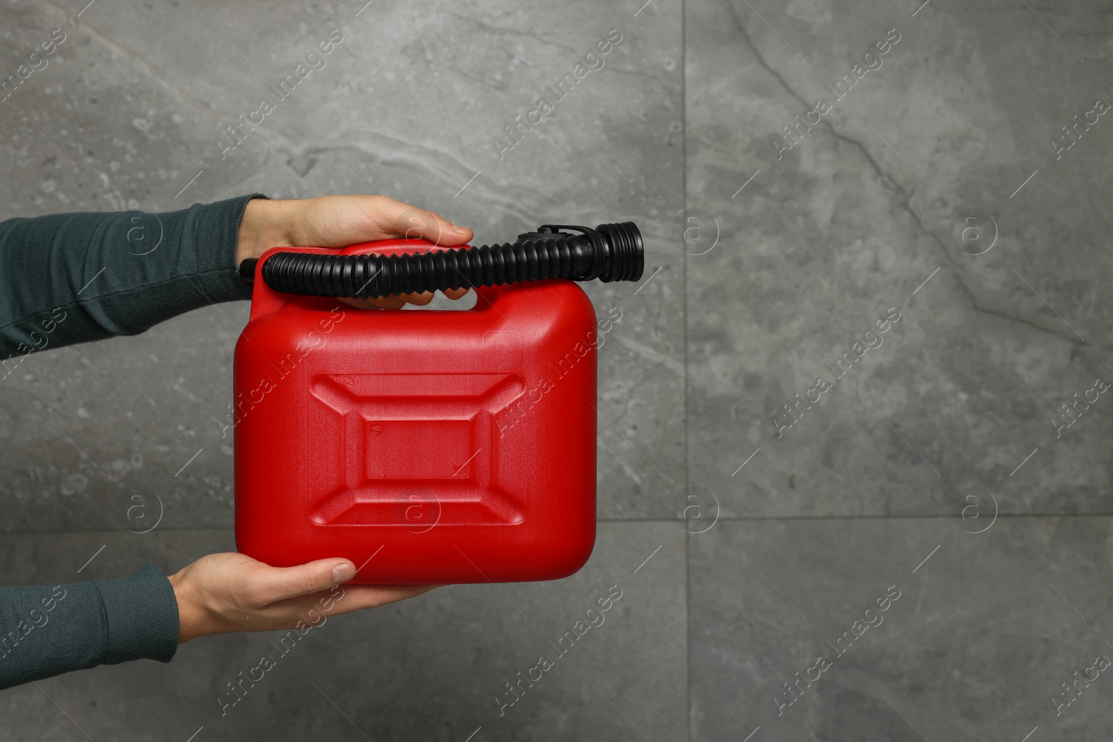 Photo of Man holding red canister near grey wall, closeup. Space for text