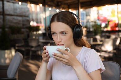 Smiling woman in headphones drinking coffee in outdoor cafe
