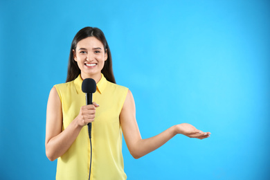 Photo of Young female journalist with microphone on blue background