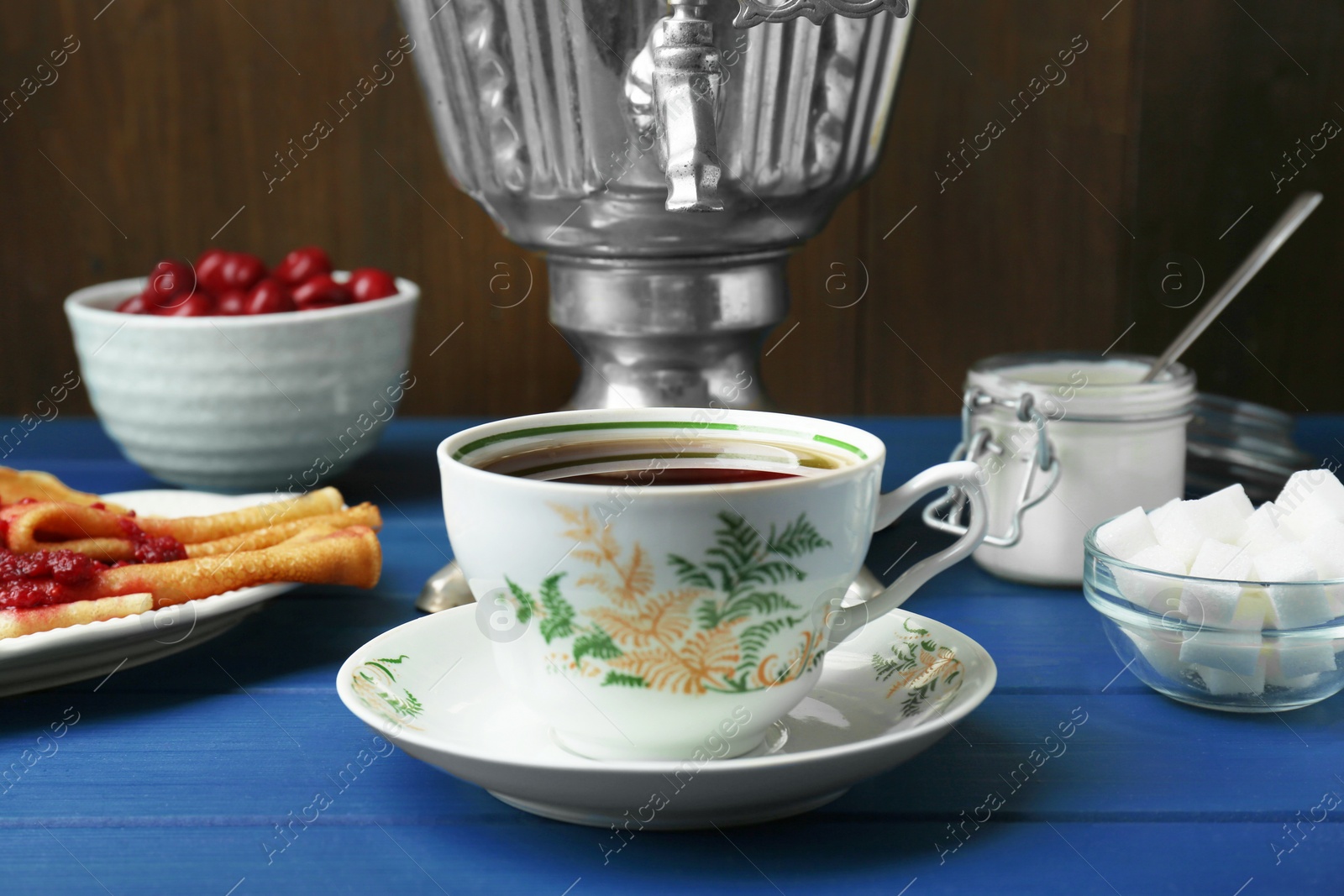 Photo of Aromatic tea, traditional Russian samovar and treats on light blue wooden table