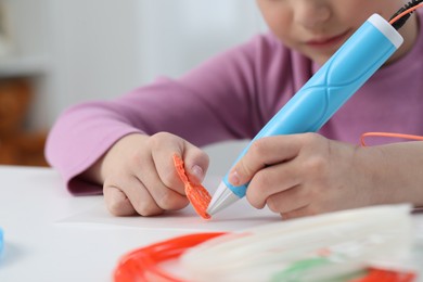 Photo of Girl drawing with stylish 3D pen at white table indoors, closeup