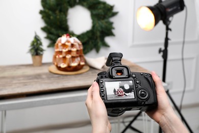Photo of Food photography. Woman with professional camera taking photo of Pandoro cake, Christmas wreath and tree on table in studio, closeup. Space for text