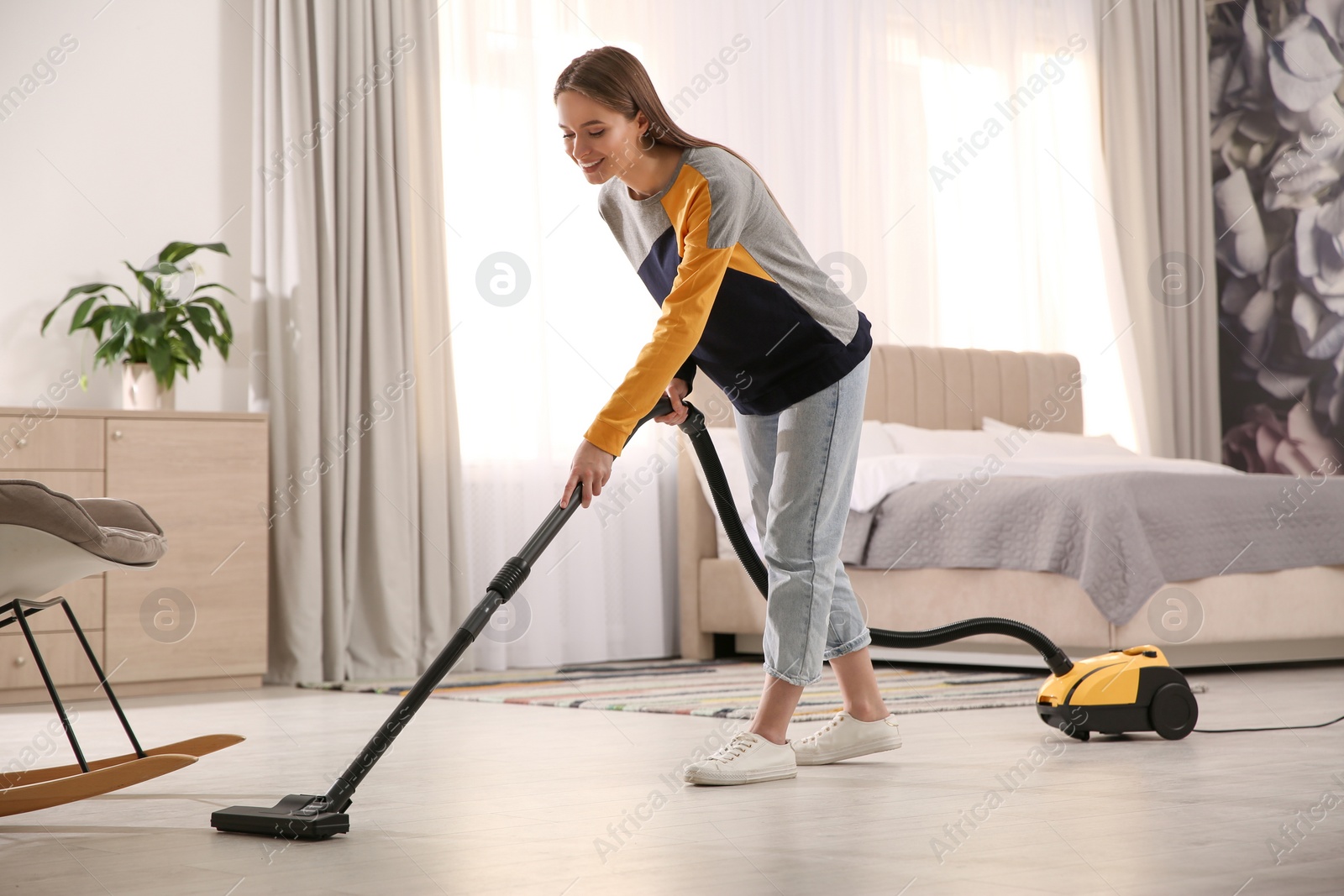 Photo of Young woman using vacuum cleaner at home