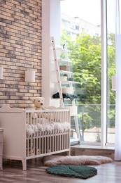 Photo of Baby room interior with crib near brick wall