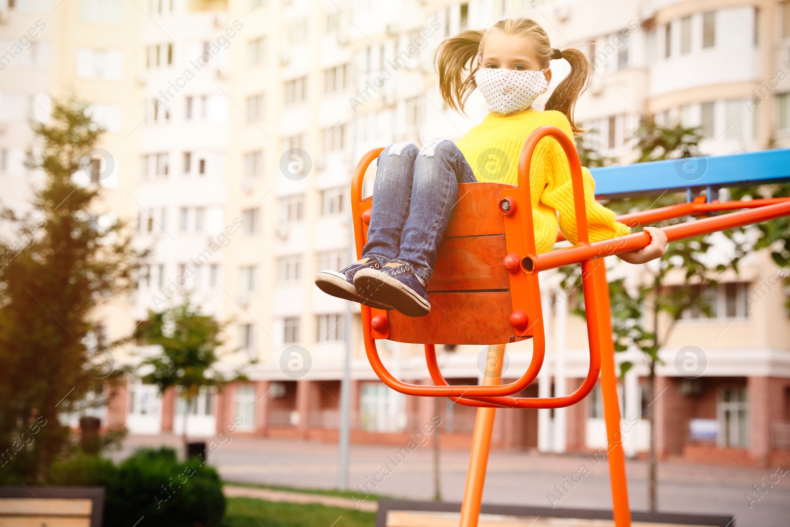 Photo of Little girl with medical face mask on playground during covid-19 quarantine