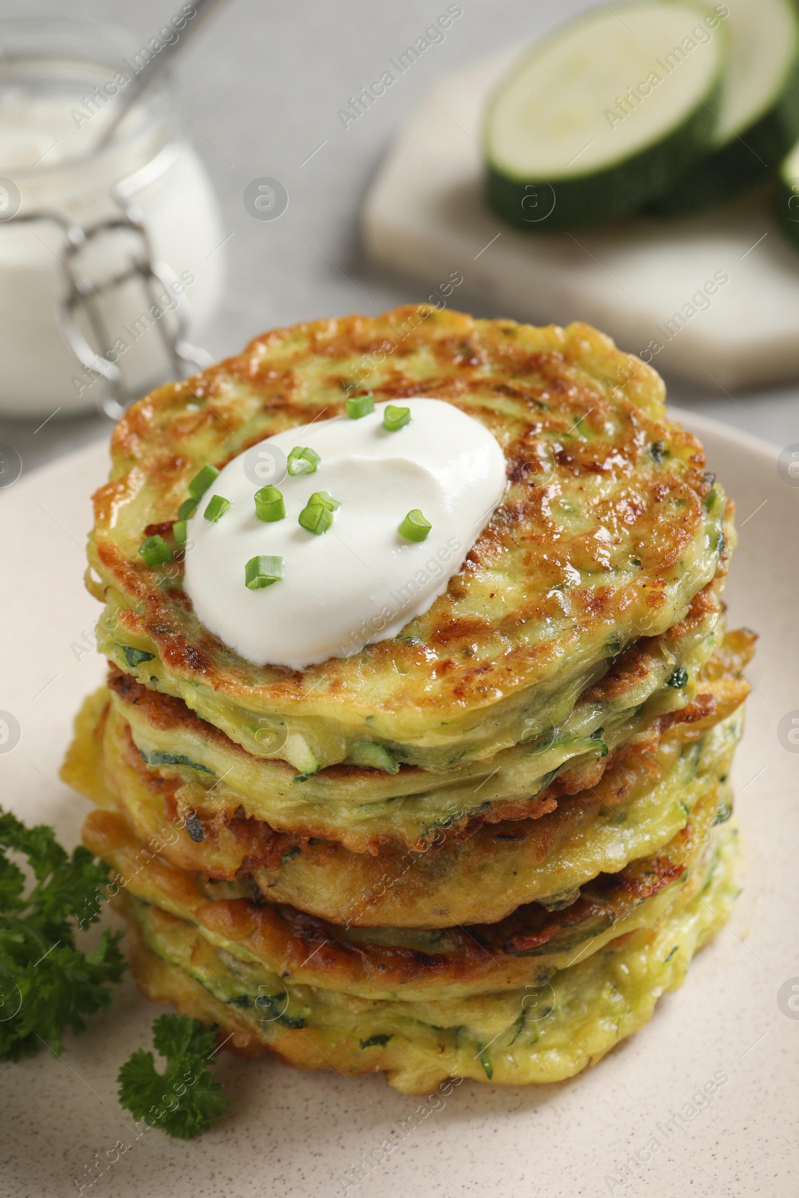 Photo of Delicious zucchini fritters with sour cream on plate