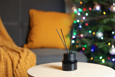Photo of Aromatic reed air freshener on white wooden side table in cozy room