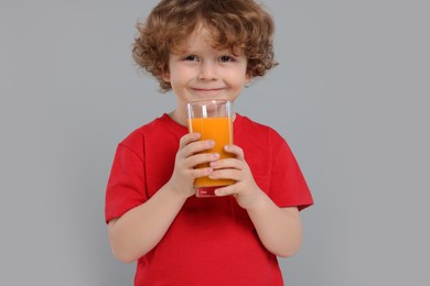 Cute little boy with glass of fresh juice on light gray background