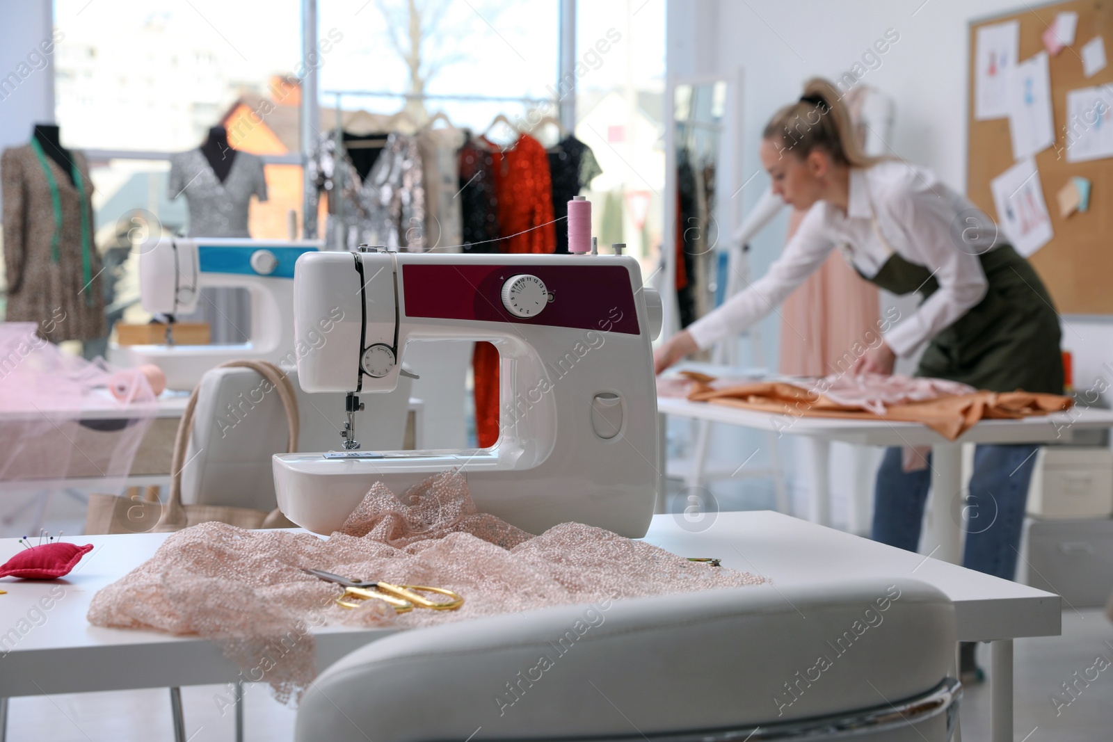 Photo of Dressmaker working in atelier, focus on table with sewing machine and accessories