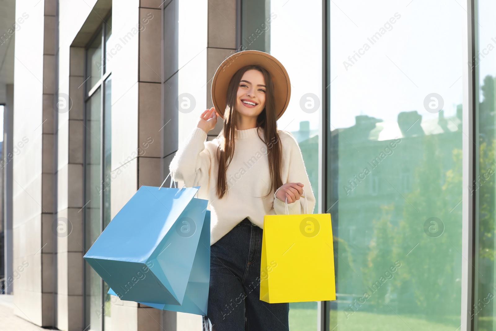 Photo of Beautiful young woman with shopping bags near building outdoors