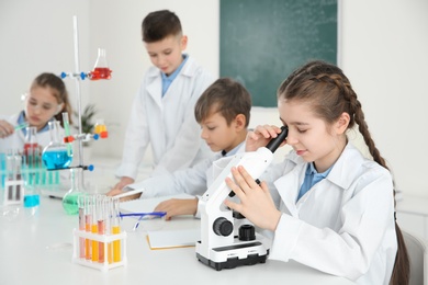 Smart girl looking through microscope and her classmates at chemistry lesson