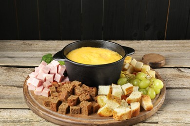 Photo of Fondue pot with melted cheese and different products on wooden table