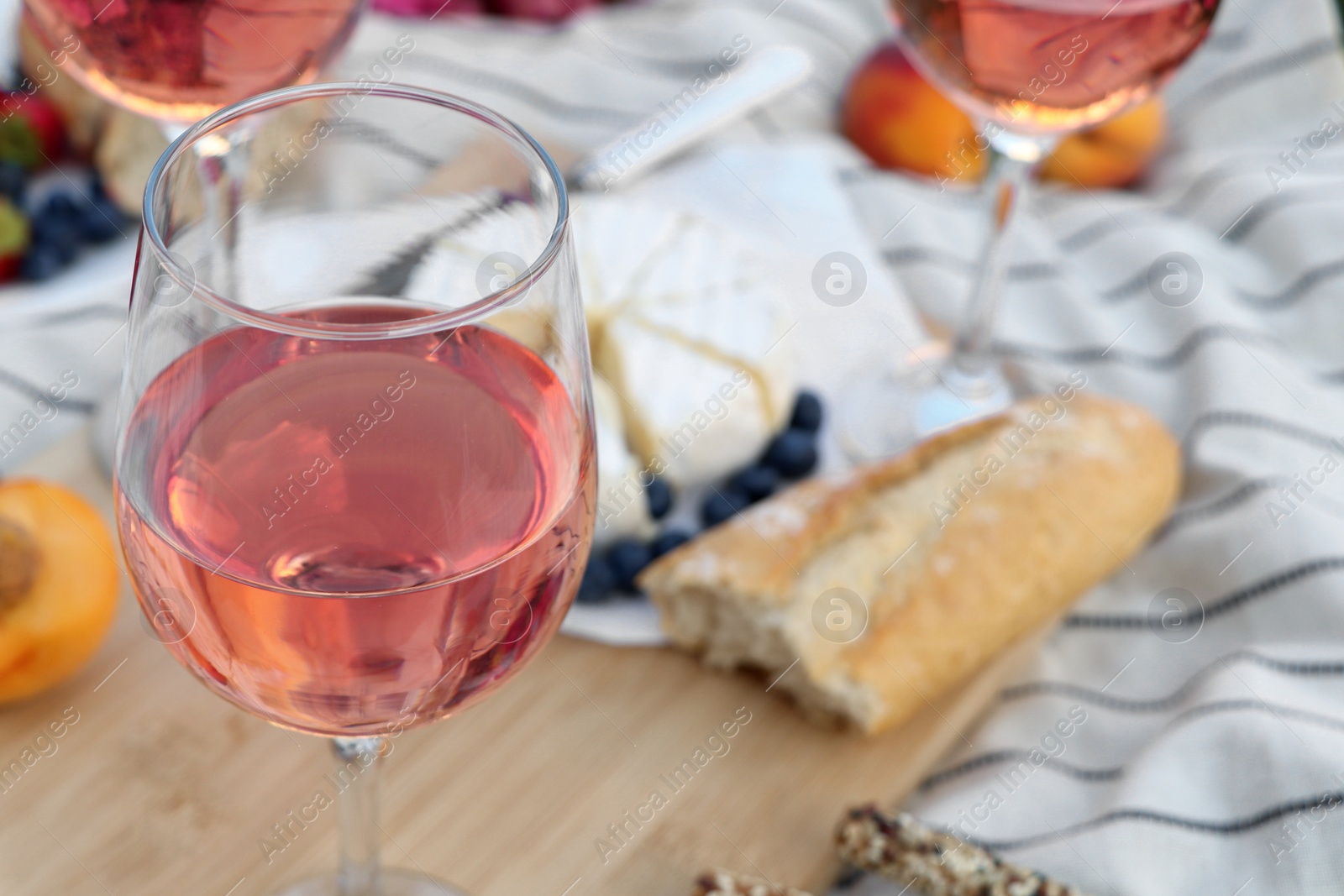 Photo of Glasses of delicious rose wine and food on white picnic blanket, closeup