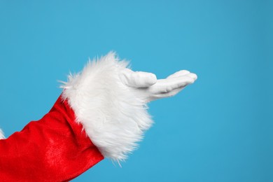 Photo of Merry Christmas. Santa Claus holding something on light blue background, closeup