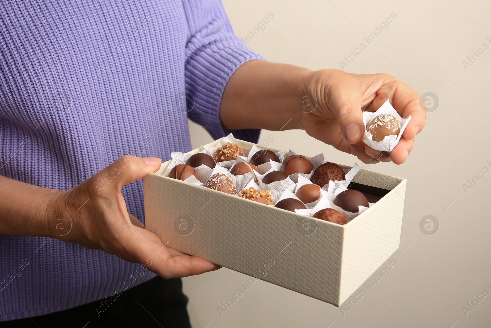 Photo of Woman taking delicious chocolate candy from box on light gray background, closeup