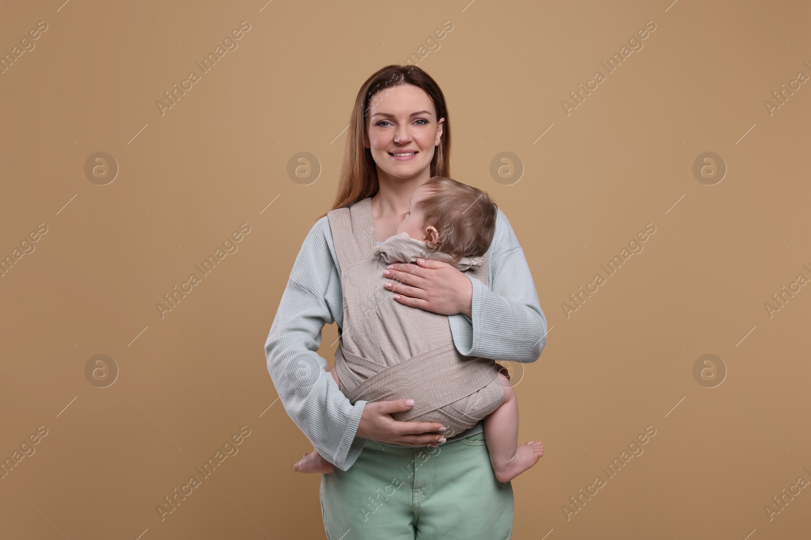 Photo of Mother holding her child in sling (baby carrier) on light brown background