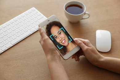 Image of African-American woman using smartphone with facial recognition system at table, closeup. Biometric verification