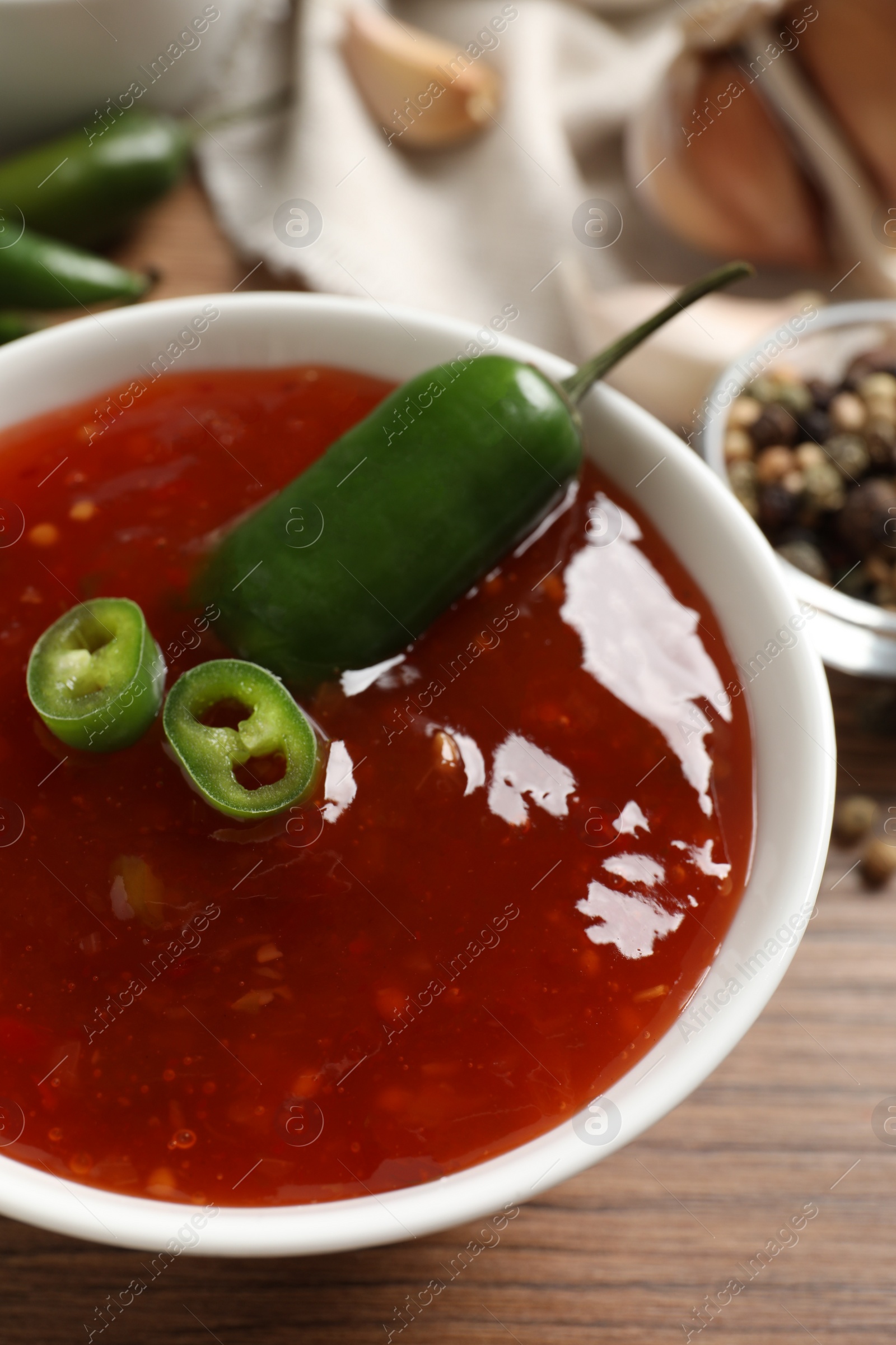 Photo of Spicy chili sauce in bowl on wooden table, closeup