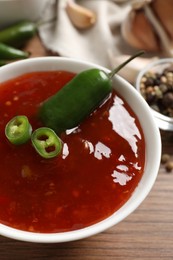 Photo of Spicy chili sauce in bowl on wooden table, closeup