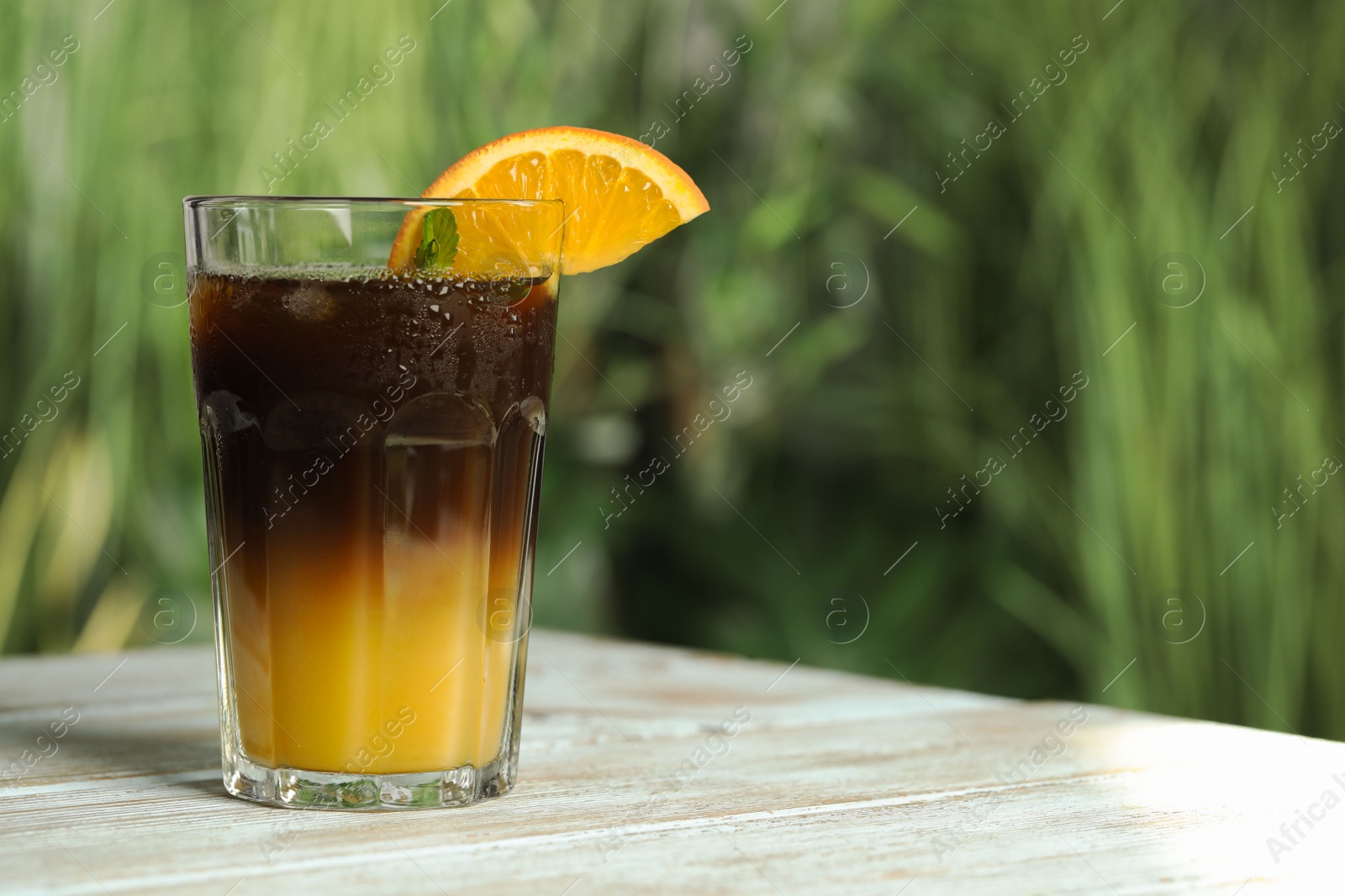 Photo of Tasty refreshing drink with coffee and orange juice on white wooden table against blurred background, space for text