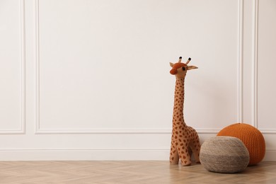 Toy giraffe and poufs near white wall indoors, space for text. Interior design