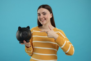 Photo of Happy woman pointing at piggy bank on light blue background