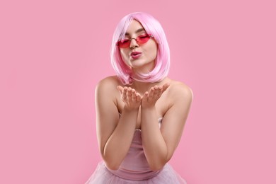 Photo of Pink look. Beautiful woman in wig and bright sunglasses blowing kiss on color background