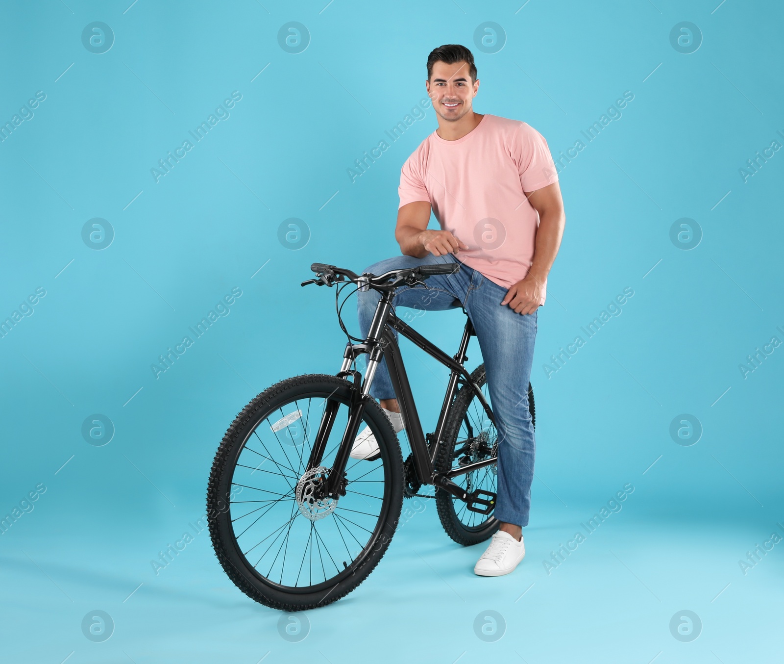 Photo of Handsome young man with modern bicycle on light blue background