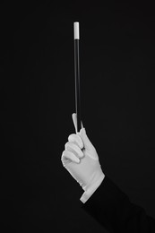 Magician holding wand on black background, closeup