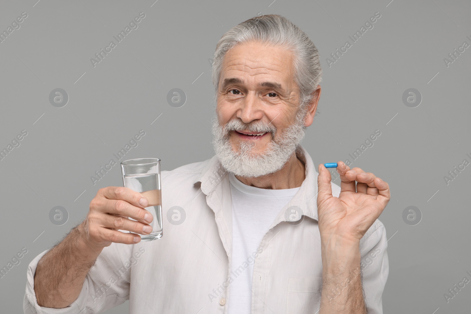 Photo of Senior man with glass of water and pill on grey background