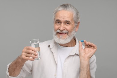 Senior man with glass of water and pill on grey background