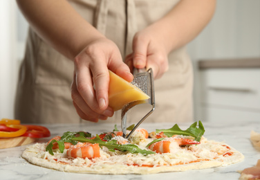 Photo of Woman grating cheese onto pizza at white marble table, closeup