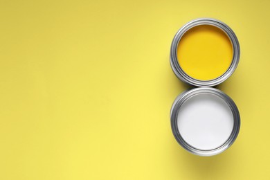 Photo of Cans with different paints on yellow background, flat lay. Space for text
